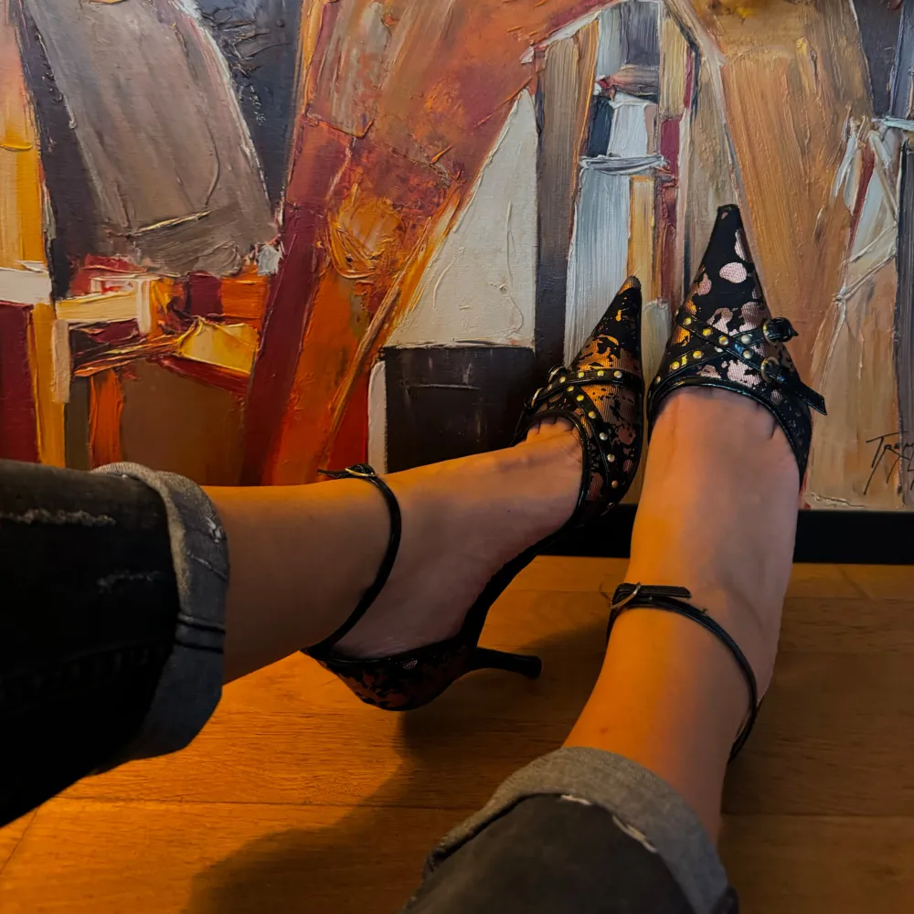 Säljer ett par eleganta svarta pumps med spetsig tå och remmar runt ankeln. Skorna har ett glittrigt mönster och små nitar som ger en extra touch av stil. Perfekta för festliga tillfällen!. Kengät.