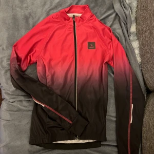 Röd och svart jacka  - Säljer en snygg röd och svart spring jacka. Den har en cool ombre-effekt från rött till svart och en dragkedja framtill. Perfekt för träning eller en casual look. Jackan är långärmad och har en normal passform.
