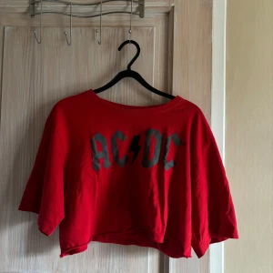 Röd AC/DC croppad tröja - Säljer en cool röd croppad tröja med AC/DC-tryck. Perfekt för rockälskare som vill ha en avslappnad och trendig stil. Tröjan har en lös passform och korta ärmar, vilket gör den perfekt för sommardagar eller festivaler. Den är i bra skick och redo för nya äventyr!
