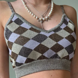 Rutig stickad topp med smala axelband - Superfin stickad kort topp med smala axelband. Toppen har ett rutigt mönster i glittrigt brons, guld, mörklila och lila. Den är tight och croppad💕originalpris ungefär 1000kr 