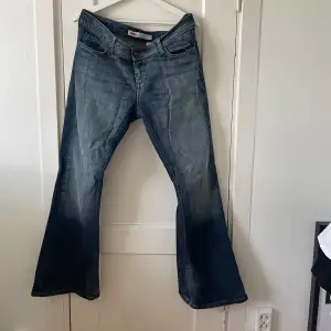 Säljer ett par snygga blå bootcut jeans från ONLY i storlek 44. De är i bra skick och har en klassisk femficksdesign med dragkedja och knapp framtill. Perfekta för både vardag och fest!