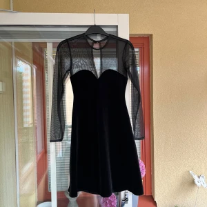 Svart klänning med meshärmar - Säljer en superfin svart klänning med meshärmar. Klänningen är i ett mjukt och glansigt material, och har en tight passform upptill med en lätt utsvängd kjol. Den har långa ärmar i genomskinligt meshmaterial som ger en cool kontrast till den annars täckande klänningen. Perfekt för fest eller en utekväll! 🖤