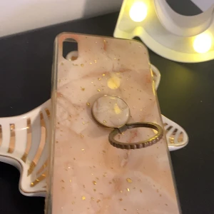 Beige mobilskal med ringhållare - Säljer ett snyggt vit mobilskal med guldiga detaljer och en praktisk ringhållare på baksidan. Skalet har en marmorerad design! 💗Perfekt för att skydda din mobil och samtidigt ha en as snygg mobil! säljer pga att jag aldrig använder den här längre! passar iPhone XS max 💘 skriv om det är något ni undrar! pris kan diskuteras😻