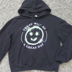 Svart hoodie med tryck - Säljer en mörkbrun hoodie med ett coolt tryck på framsidan som säger 'Today will be a great day' och en smiley. Den är perfekt för en chill dag eller när du vill ha något bekvämt och stiligt. Hoodien har en normal passform och är gjord av mjukt material. Den har en klassisk  justerbar huva med dragsko.