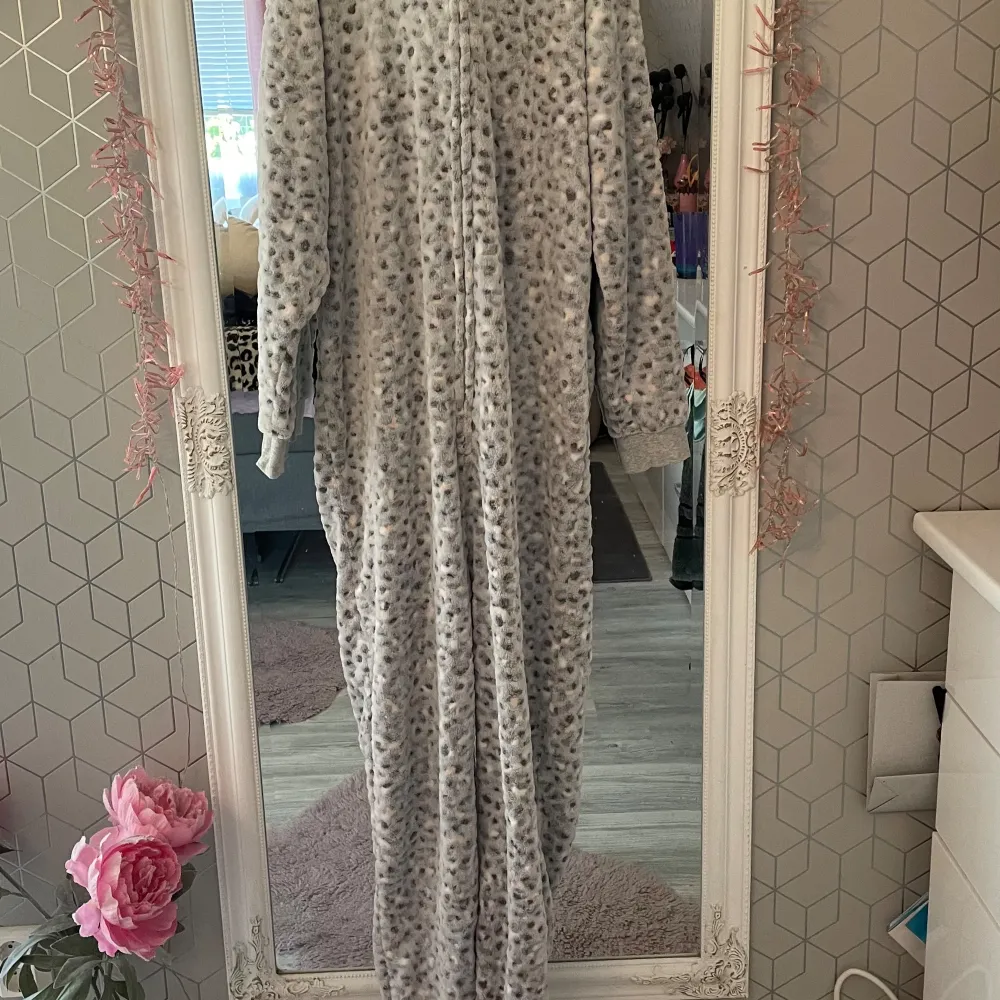 Säljer en supermysig grå leopardmönstrad onesie från Lindex. Den har en söt huva med ögon och öron, och är gjord av mjuk fleece. Perfekt för kalla dagar när du bara vill mysa hemma. Den har en dragkedja framtill och är i storlek 170, vilket passar för 14+ år. Använd några gånger men i bra skick!. Muu.