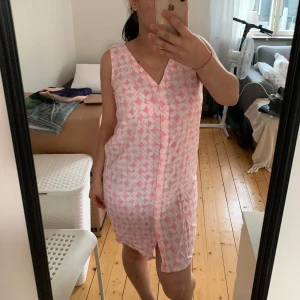 Rosa ärmlös klänning med mönster - Säljer en superfin rosa klänning med vitt mönster. Den är ärmlös och har en knappdetalj framtill. Perfekt för sommaren och passar både till vardags och fest. Klänningen är i nyskick och är väldigt bekväm att ha på sig.