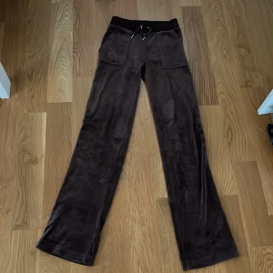 Bruna mjukisbyxor från Juicy Couture - Säljer ett par bruna mjukisbyxor från Juicy Couture i storlek XXS. Byxorna är med snörning och två fickor fram och bak. De är supermjuka och perfekta för en avslappnad look. Passar perfekt för mysiga hemmakvällar eller en chill dag ute. 🧡 