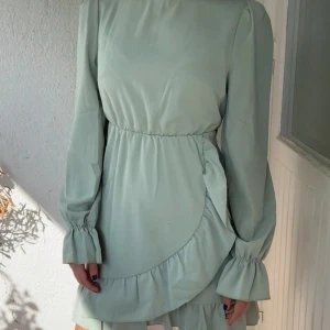 Klänning  - Sparsamt använd pastellgrön klänning med långa ärmar och volang nertill samt knyta bak.