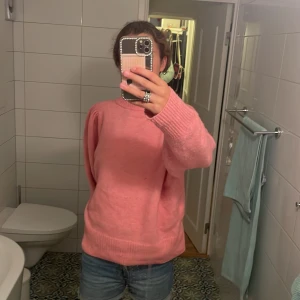 Rosa stickad tröja - Säljer en supermysig rosa stickad tröja. Den är perfekt för kyliga dagar och har en avslappnad passform. Tröjan har långa ärmar och ribbade muddar vid ärmslut och nederkant. Perfekt för både höst och vinter!