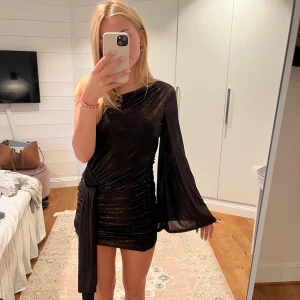 Nyårs klänning  - Svart men gluttar i guld och man kan bestämma hur lång bandet som hänger ska vara genom att stoppa in och ut från en stor ficka 