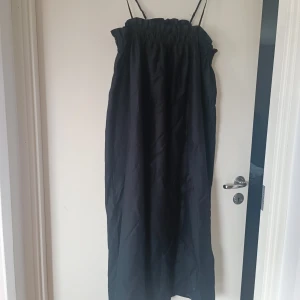 Svart långklänning från 157 - Säljer en elegant svart långklänning från Lager 157. Klänningen har smala axelband och en elastisk överdel som ger en bekväm passform. Perfekt för både vardag och festliga tillfällen!