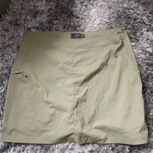 Beige kjol från High Mountain - Säljer en snygg beige kjol från High Mountain. Den är perfekt för en avslappnad dag ute eller en promenad i naturen. Kjolen har en enkel design med en liten ficka på sidan och är gjord i ett lätt och bekvämt material.