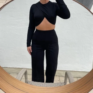 Svart croppad topp från NLY One - Säljer en svart croppad topp från NLY One. Den har en cool omlott-design framtill och långa ärmar. Perfekt för en utekväll eller fest! Toppen är tight och ger en snygg siluett. Liten i storleken