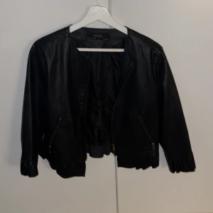 Svart skinnjacka från Zara Basic - Snygg svart skinnjacka från Zara Basic med volangdetaljer vid nederkanten. Ärmarna är trekvarts, skitsnygg nu till våren! Storlek L men passar mer en S. 