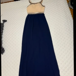 Elegant långklänning med pärldetaljer - Säljer en elegant långklänning från Chiara Forthi Milano, med en beige överdel och marinblå kjol. Klänningen har vackra pärldetaljer runt halsringningen och midjan. Perfekt för en speciell kväll! Storlek XS 💙