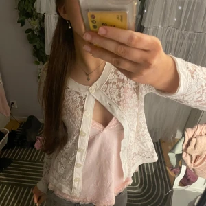 Vit spetskofta med knappar - Säljer en elegant vit spetskofta med knappar framtill. Koftan har långa ärmar och en rund halsringning. Perfekt för att lägga till en söt touch till din outfit. Passar bra över en topp eller klänning.