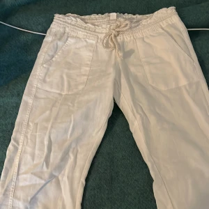 Vita linne byxor från Roxy - Säljer ett par vita byxor från Roxy med elastisk midja och snörning. Byxorna har en avslappnad passform och är perfekta för en ledig stil. Säljer för att de är för korta på mig, är 168. Skulle säga de passar nån som är 155-162.