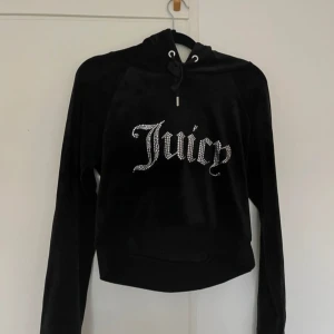 Svart hoodie och byxor från Juicy Couture - Säljer en svart hoodie från Juicy Couture i mjukt sammetstyg. Den har långa ärmar och en glittrig Juicy-logga på framsidan. Perfekt för en avslappnad och stilren look.