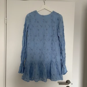 Ny Ljusblå klänning från NA-KD - Charmig ljusblå klänning med broderade blommor och volangdetaljer. Klänningen har en djup v-ringning och knytband i ryggen. Långärmad design med en luftig passform som ger en romantisk känsla. Perfekt för vårens och sommarens tillfällen. Nypris 799kr