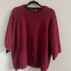 Vinröd stickad tröja - Mysig vinröd stickad tröja med en avslappnad passform. Perfekt för kyliga dagar med sin varma och bekväma design. Tröjan har en rund halsringning och trekvartsärmar.