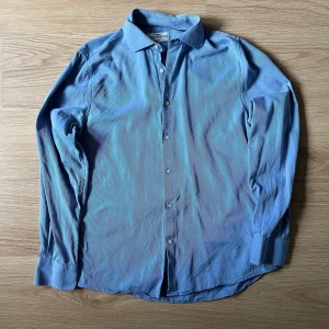 Blå skjorta från Hampton Republic - Snygg blå skjorta från Hampton Republic i slim fit. Skjortan har ett diskret randigt mönster och knappar framtill. Perfekt för en stilren look.