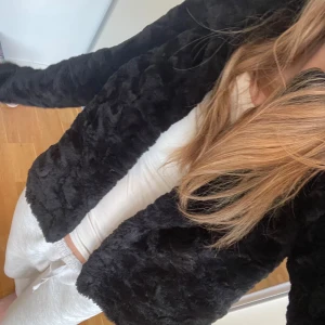 Svart pälsjacka - S-M. Säljer en mysig svart pälsjacka med lång ärm. Jackan har en fluffig textur och är perfekt för kyligare dagar, en sen sommarkväll! Den har en enkel design utan synliga detaljer som knappar.