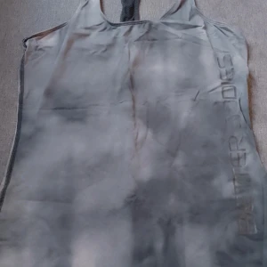 Grå linnetopp från Better Bodies - Säljer en grå träningstopp från Better Bodies. Toppen är ärmlös och har en sportig design med ett diskret mönster. Perfekt för träning eller en avslappnad dag. Trådsläpp på nedersta dubbelsömmen.