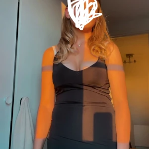 Svart Rebecca Stella klänning  - Snygg svart klänning med smala axelband och djup urringning. Perfekt för en kväll ute eller en speciell tillställning. Den har en figurnära passform som framhäver silhuetten.