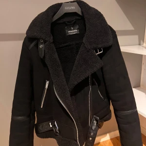 Svart jacka från Stradivarius - Snygg svart jacka från Stradivarius med en mysig fuskpälsfoder. Jackan har dragkedja och bälte i midjan för en cool look. Perfekt för kyligare dagar med sin stilrena design och praktiska detaljer.