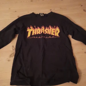 Svart långärmad Thrasher tröja - Säljer en svart långärmad tröja från Thrasher med den ikoniska loggan i eldflammor på framsidan. Står ej ngn storlek i men passar en 12-13åring, ca strö 158/164. En liten grå prick finns långt ner på magen, 0,5x0,5 cm.