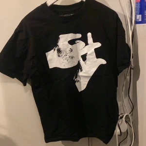 Svart t-shirt med tryck från Playboi Carti - Säljer en svart t-shirt med coolt vitt tryck fram och texten 'HOLE LOTTA RED' på baksidan. Perfekt för fans av Playboi Carti. T-shirten har en normal passform och korta ärmar.