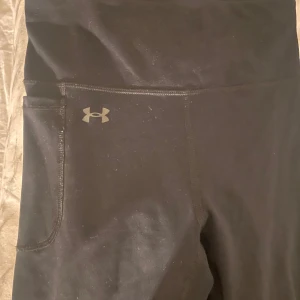 Svarta leggings från Under Armour - Snygga svarta leggings från Under Armour med hög midja och en liten logga på sidan. Perfekta för träning eller en avslappnad dag. De har en tight passform och är gjorda i ett stretchigt material för bästa komfort.