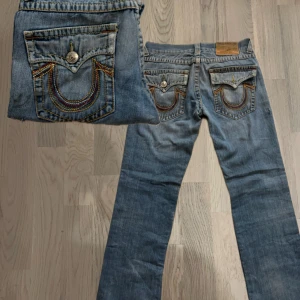 True Religion Rainbow World Tour - Snygga blå jeans från True Religion med ikonisk broderad detalj på bakfickorna. De har en klassisk femficksdesign och en bekväm passform. Perfekta för en avslappnad stil. TAR BUD BA O SKICKA ! length: 106 width: 41 leg openingin 22