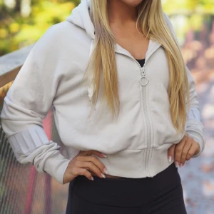 hoodie med dragkedja - Snygg hoodie med dragkedja och huva från Puma, influensern Kenza’s kollektion. Den har ribbade muddar och en croppad passform som ger en modern look. Perfekt för träning, aktiviter och i vardagen🤍