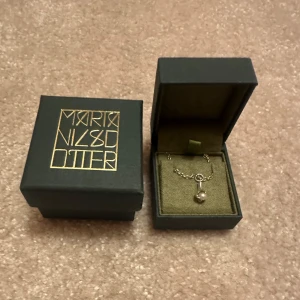 Halsband med pärla från Maria Nilsdotter - Elegant halsband från Maria Nilsdotter med en fin kedja och ett hängsmycke prytt med en pärla. Perfekt för att ge en stilren touch till din outfit. Kommer i en snygg förpackning. Kedjan är i storlek 40 och detta halsband är väldigt eftersökt❤️