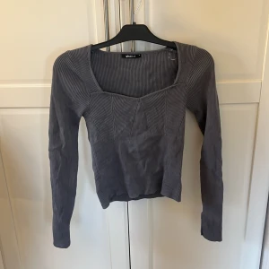 Grå ribbad tröja från Gina - Snygg grå ribbad tröja från Gina med långärmad design och fyrkantig halsringning. Perfekt för en stilren look. Passar bra till både jeans och kjol.