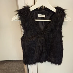 Svart pälsväst från H&M - Snygg svart pälsväst från H&M som ger en trendig look. Perfekt för att lägga till lite extra stil till din outfit. Västen är ärmlös och har en mjuk känsla.