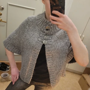 Grå stickad kofta med korta ärmar - Säljer en mysig grå stickad kofta med stora dekorativa knappar framtill. Koftan har korta ärmar och en ribbad krage som ger en stilren look. Perfekt för kyliga dagar när du vill ha något bekvämt och snyggt. Så sjukt snygg!!!!!! Passar mig som brukar ha XS och S, pasar även M🩷🩷🩷 SÅ trendig!! Är öppen för prisförslag!