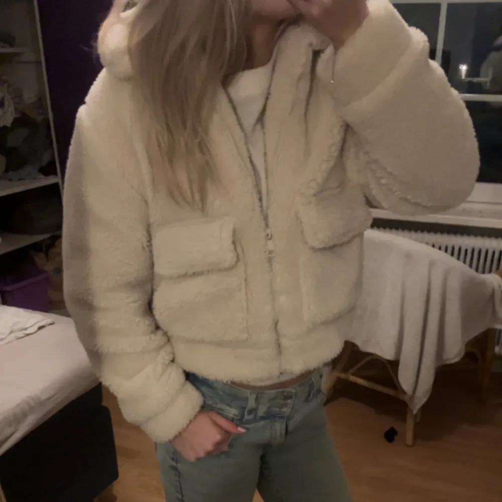 Mysig beige teddyjacka med dragkedja och huva. Jackan har två stora fickor framtill och är perfekt för kyliga dagar. Den är både stilren och bekväm, vilket gör den till ett måste i garderoben.. Takit.