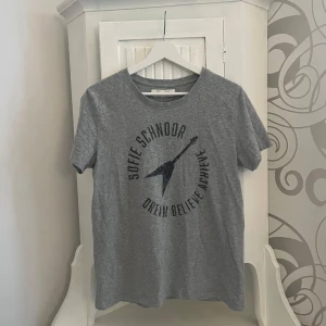 Grå t-shirt från Sofie Schnoor - Snygg grå t-shirt från Sofie Schnoor med tryck framtill. T-shirten har en normal passform och är kortärmad, perfekt för en avslappnad stil. Tillverkad i mjukt material för extra komfort.