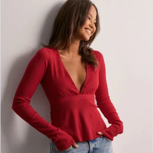 Röd ribbad topp med knytband - Snygg röd ribbad topp med v-ringning och långa ärmar. Toppen har ett knytband i ryggen som ger en fin passform. Från Nelly och helt slutsål överallt🥰