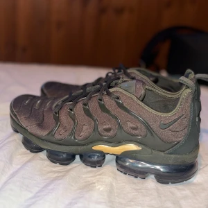 Nike Air Vapormax plus i mörkgrön med guld detaljer - Säljer ett par Nike Air Vapormax i en snygg mörkgrön och guld färgkombination. Skorna har en unik bubbelsula för extra komfort och stil. Perfekta för både träning och vardag. De har snörning och en diskret Nike-logga på sidan. Storlek 45 men passar även 43-42 helt par nya skor använda 3-4 gånger. Ny pris på dessa skor är 2100kr 