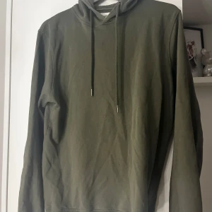 Olivgrön hoodie från Bread & Boxers - Säljer en stilren olivgrön hoodie från Bread & Boxers i storlek M. Den har en klassisk design med dragsko i huvan och långa ärmar. Perfekt för en avslappnad look. Pris går att diskutera 