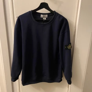 Mörkblå sweatshirt från Stone Island - Hej, jag säljer en sweatshirt från Stone Island som är mörkblå. Tröjan är väldigt bekväm och i toppskick  och har till och med taggen kvar på sig. En stone Island påse ingår men den har tyvärr några enstaka hål. Pris kan självklart diskuteras, mvh Emil. 
