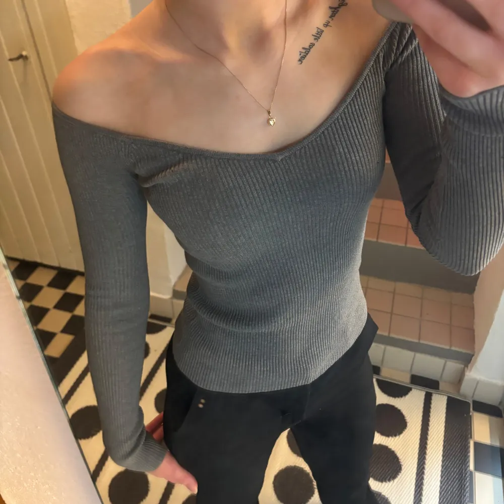 Snygg grå ribbad tröja med offshoulder-design och långa ärmar. Perfekt för en stilren look.. Neuletakit & Villapaidat.