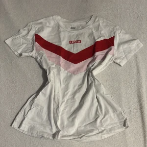 Vit t-shirt från Levi's med röd och rosa design - Säljer en snygg vit t-shirt från Levi's med ett coolt rött och rosa mönster över bröstet. Perfekt för en avslappnad stil. T-shirten har korta ärmar och rund halsringning. Säljer även likadan fast i svart🫶