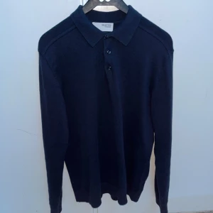 Långärmad piké  - Säljer en stilren mörkblå pikétröja från Selected Homme. Tröjan har långa ärmar och en klassisk krage med knappar framtill. Perfekt för en avslappnad men ändå uppklädd look.