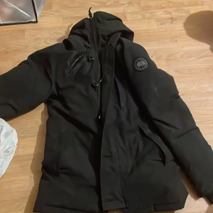 Svart jacka från Ganada goose - Säljer en svart canada goose Black Label Heritage den är använd ca10 gånger så den är i stort sätt oanvänd så den är som ny det är storlek xs men skulle säga att den sitter som M/L ny pris ligger den på 20750