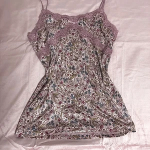 Blommig linne med spetsdetaljer - *japanska märker*.                                                          Säljer en superfin blommig linne med spetsdetaljer i en mjuk rosa nyans. Perfekt för sommardagar eller en avslappnad vårlook. Linnet har smala axelband och ett vackert blommönster i olika färger. 