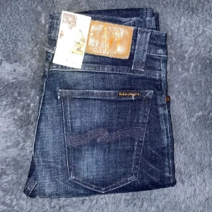 Mörkblå jeans från Nudie Jeans - Snygga mörkblå jeans från Nudie Jeans med en klassisk femficksdesign. De har en straight passform och är tillverkade i slitstarkt denim. Perfekta för en stilren look. Helt nya! (Bilderna är inte mina de är från Mella shop)